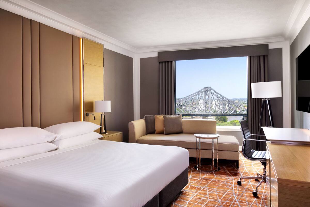 Ein Hotelzimmer mit einem großen Bett, einer Sitzecke, einem Schreibtisch und Blick auf eine Brücke sowie die Stadtlandschaft.