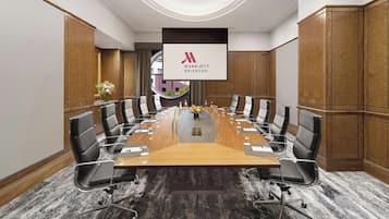 Een vergaderzaal met een lange tafel, zwarte stoelen en een groot scherm waarop het logo van Marriott Brisbane staat.