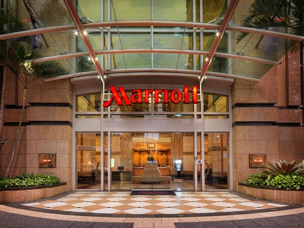 A Marriott hotel entrance with a glass facade, a checkered floor pattern, and a reception desk visible inside.