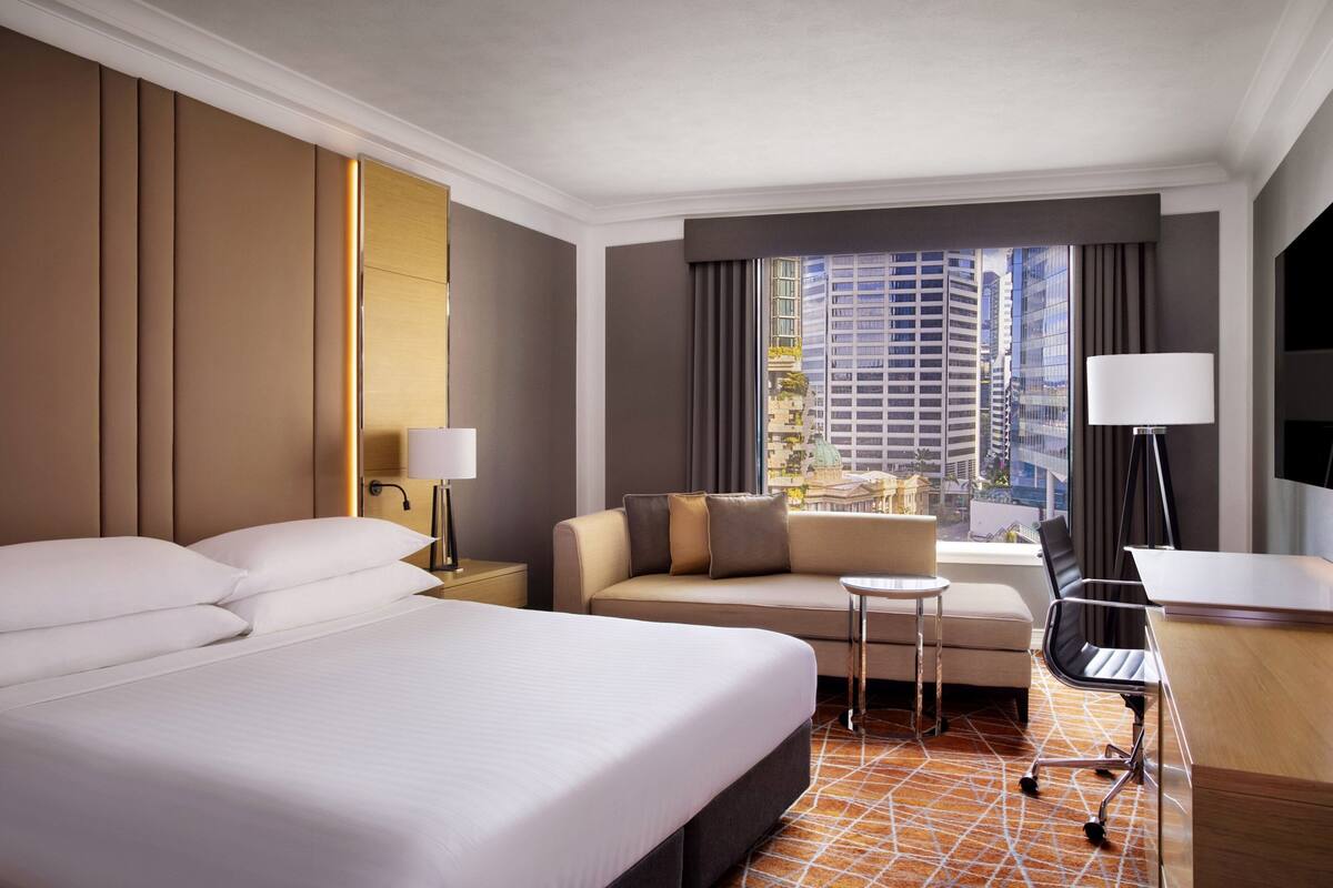 Ein Hotelzimmer mit einem großen Bett, einem Sofa, einem Schreibtisch und Blick auf die Stadtlandschaft.