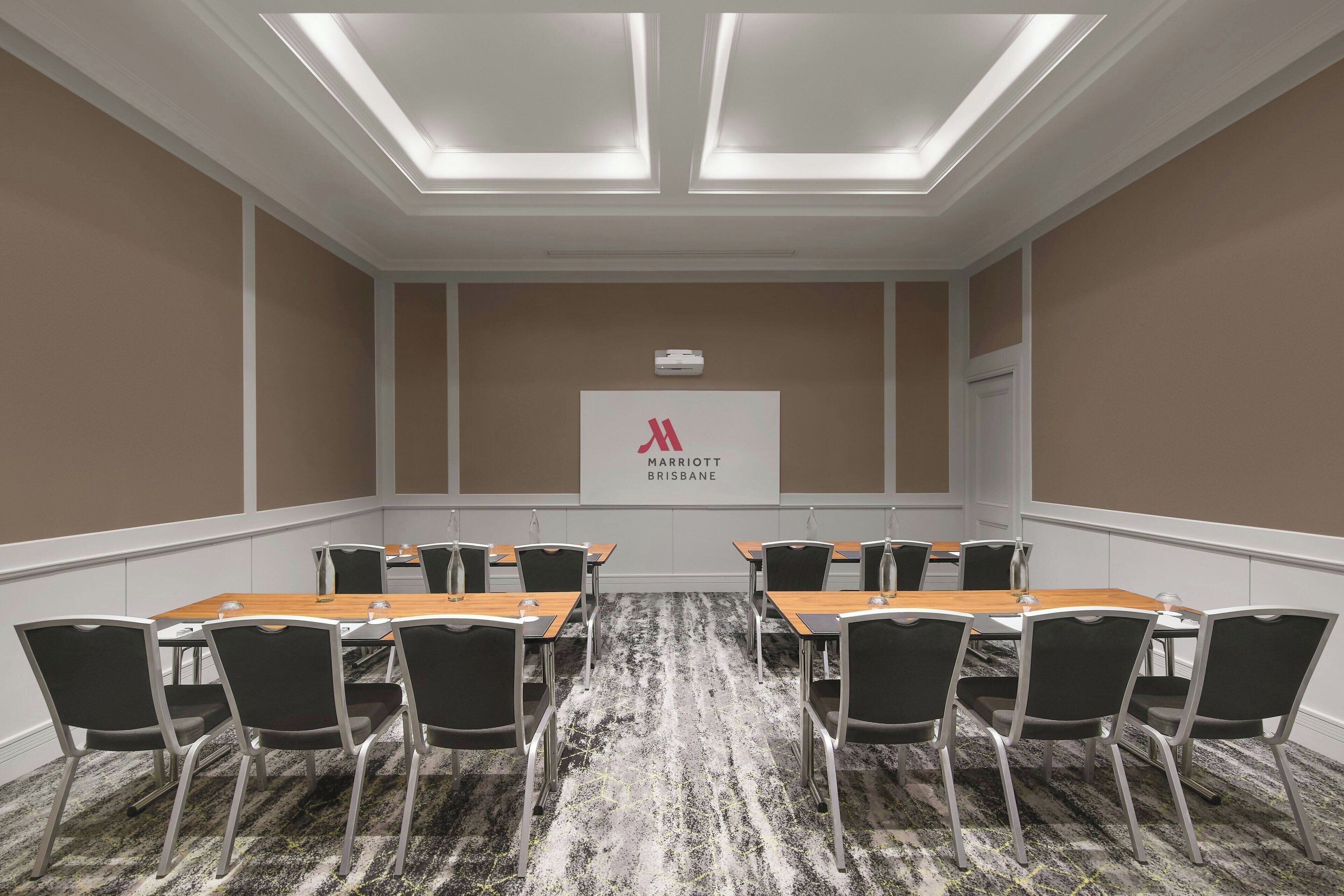 Un salón de conferencias con una larga mesa, sillas y un techo con tragaluces. Se observa un cartel con el logotipo de Marriott Brisbane en la pared.