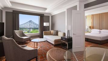 A hotel room with a sofa, armchairs, a small table, a bed, and a view of a bridge.