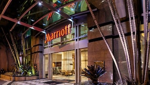 Entrada de un hotel Marriott con fachada de vidrio, piso a cuadros y plantas de interior.