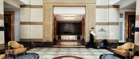 A lobby with a checkered floor, two sofas, a reception desk, and a large chandelier.