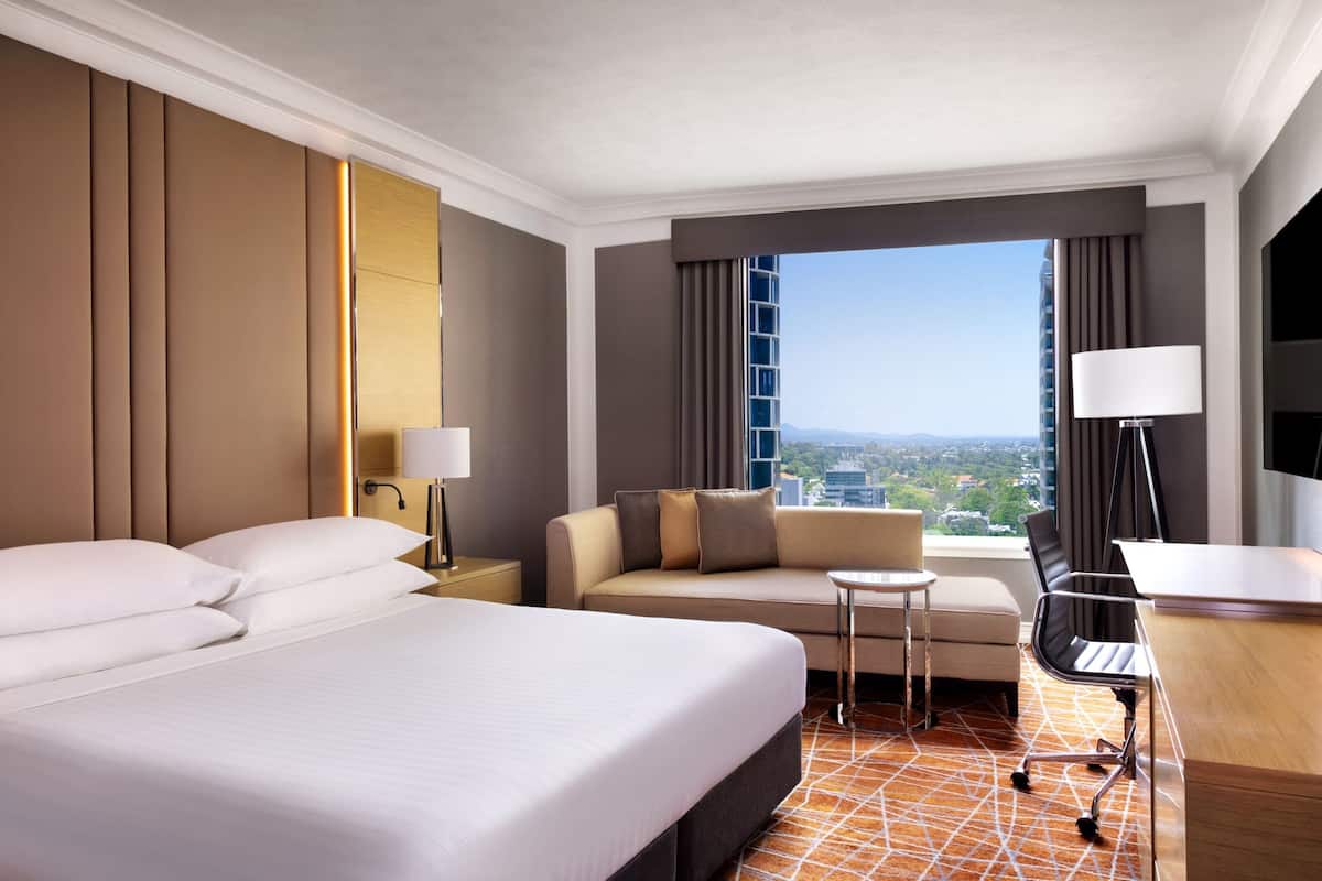 Ein Hotelzimmer mit einem großen Bett, einer Sitzecke, einem Schreibtisch und Blick auf die Stadt.