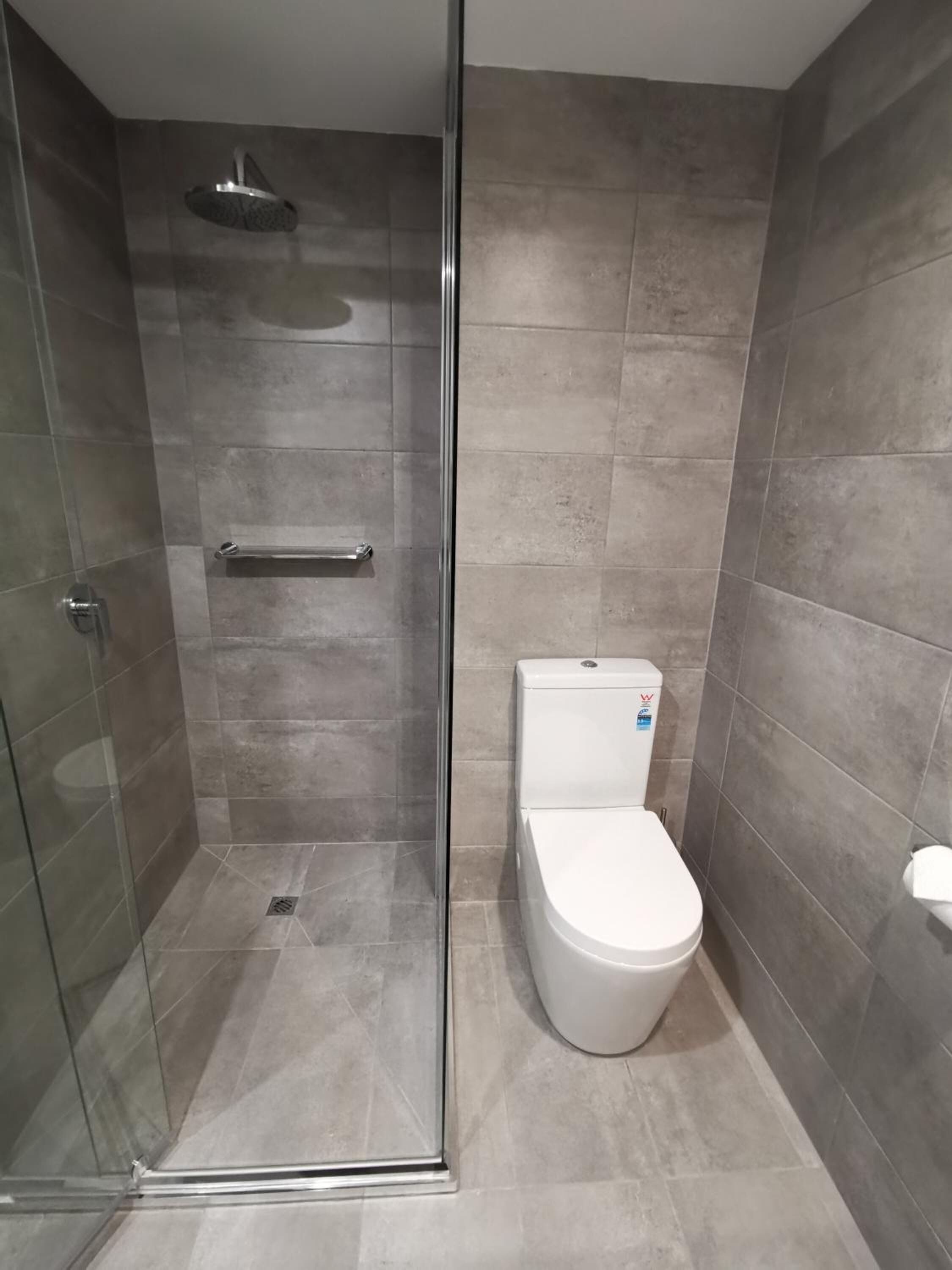 A modern bathroom with a glass-enclosed shower, a toilet, and a towel rack.