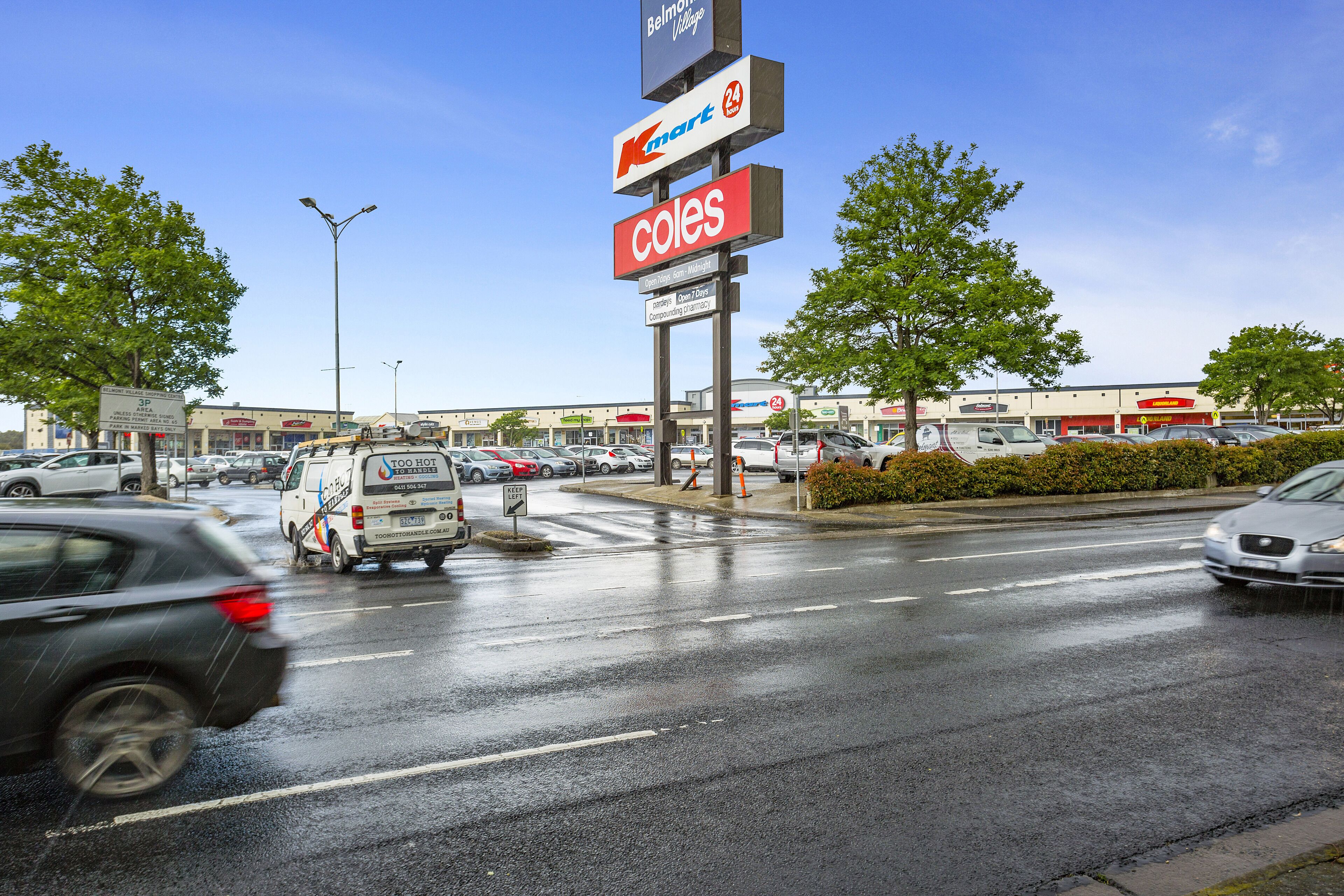 Zona comercial con letreros de Kmart y Coles, varios automóviles y una calle mojada.