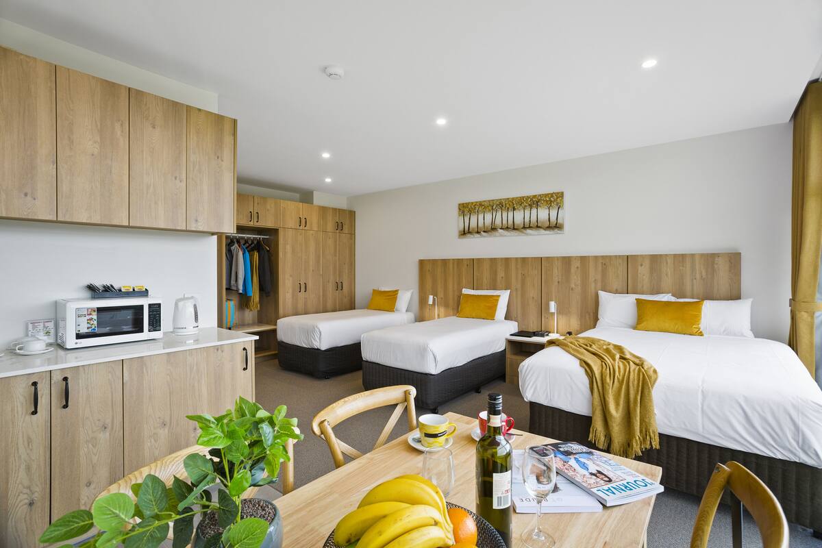 A hotel room with two beds, a dining area with a table, and a kitchenette.