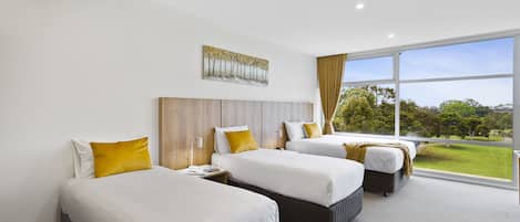 A hotel room with three beds, a large window with a view of the outdoors, and a painting on the wall.