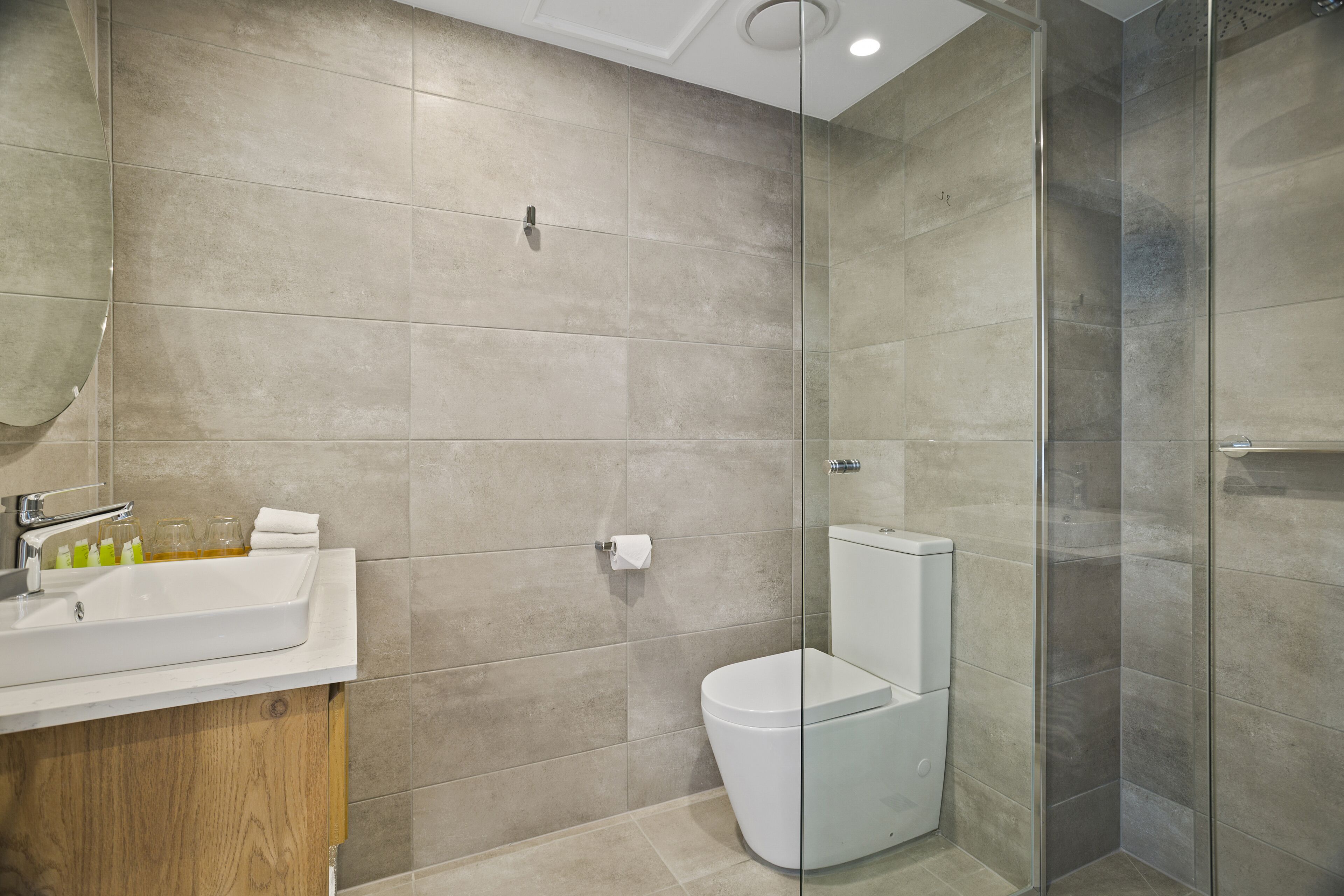 Un baño moderno con cabina de ducha de vidrio, un lavabo blanco con artículos de aseo y un inodoro.
