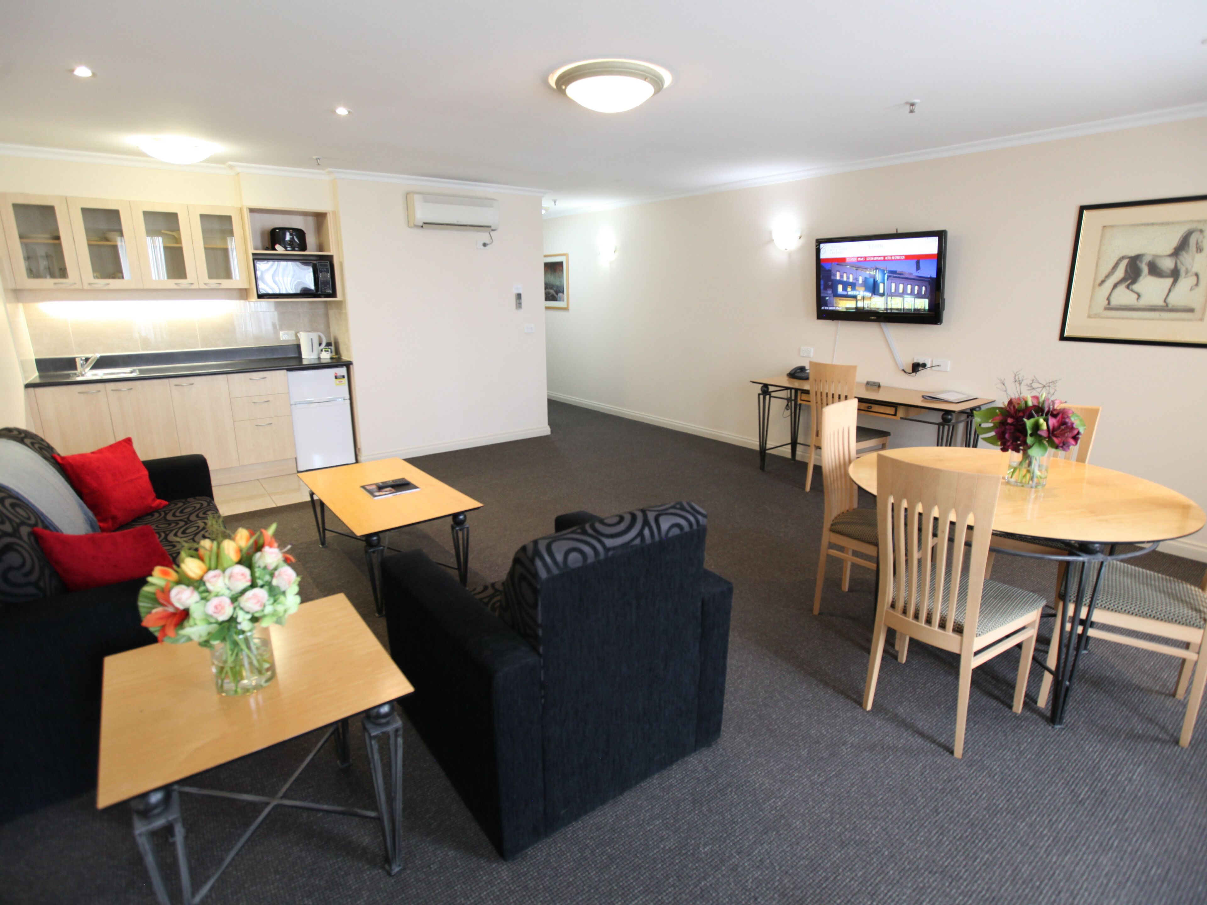 A compact living space with a kitchenette, a dining area, and a TV mounted on the wall.