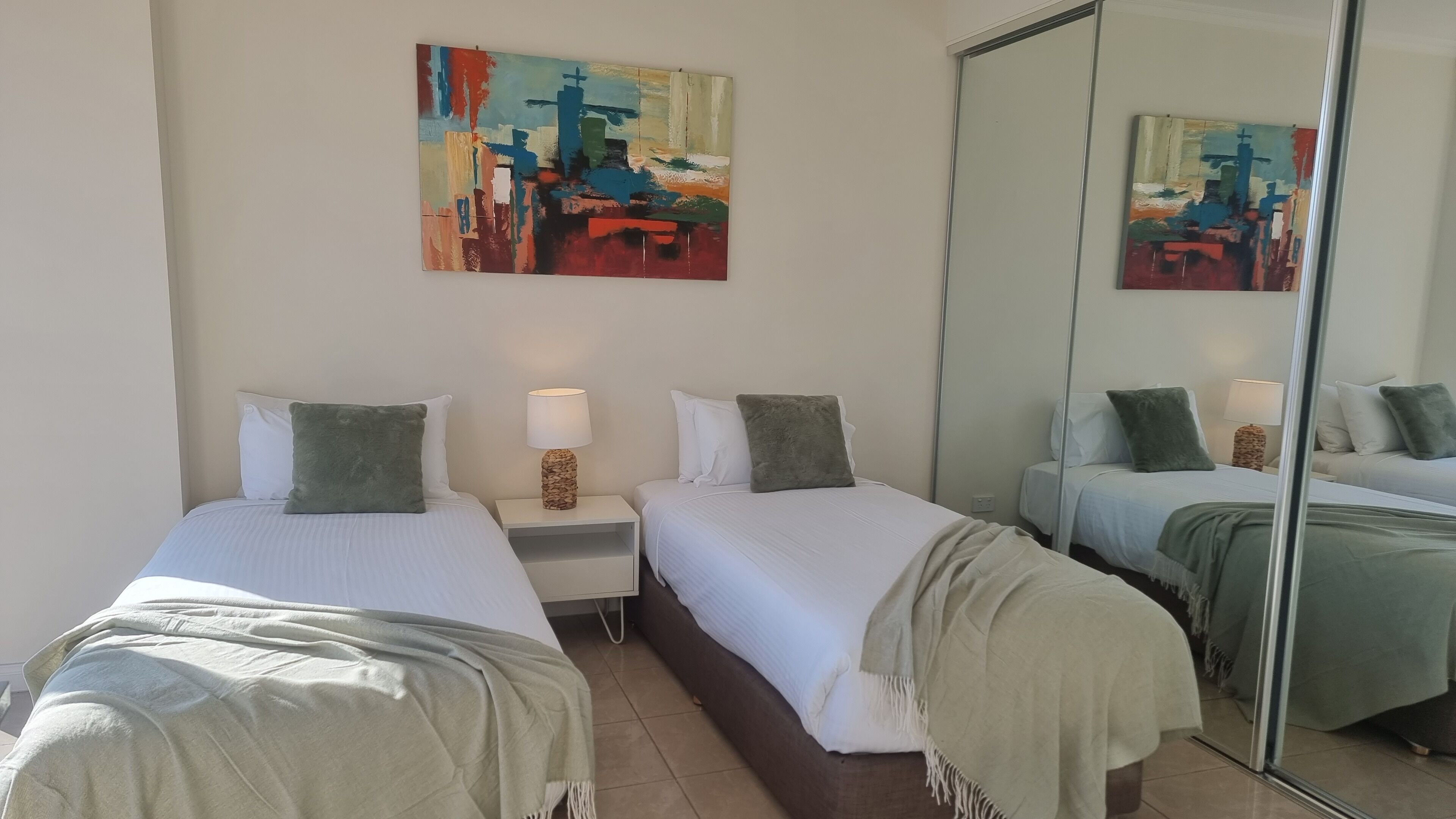 A hotel room with two beds, a large mirror, and a painting on the wall.