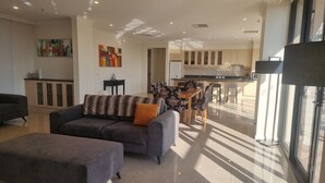 A modern living room with a grey sofa and ottoman, a dining area with patterned chairs, and a kitchen with wooden cabinets. - Melbourne Metropole Central (Fitzroy)