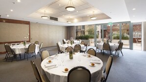 A conference room with round tables, chairs, and a large window with an exit sign. - Melbourne Metropole Central (Fitzroy)