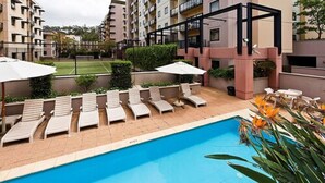 A swimming pool with sun loungers and umbrellas, surrounded by apartment buildings. - Nesuto Mounts Bay (Perth)