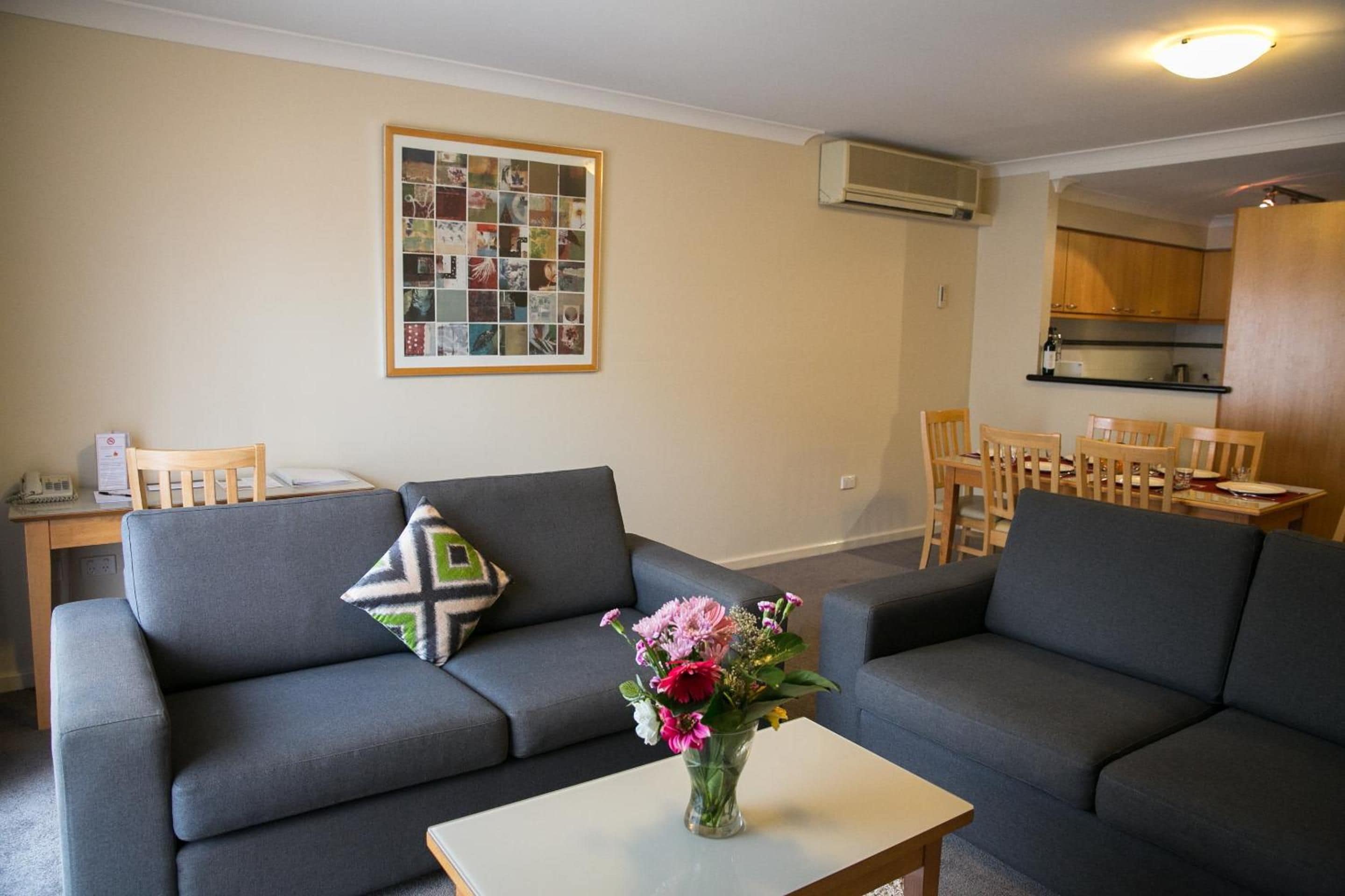 A living room with a grey sofa, a coffee table with a vase of flowers, and a framed collage on the wall.