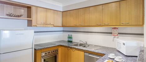 A compact kitchen with wooden cabinets, a built-in oven, a microwave, and a sink.