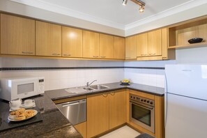 A modern kitchen with wooden cabinets, a stainless steel sink, a microwave, a dishwasher, and an oven.