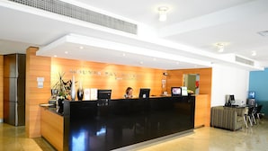 A hotel reception desk with a modern design, a receptionist, and a computer. - Nesuto Mounts Bay (Perth)