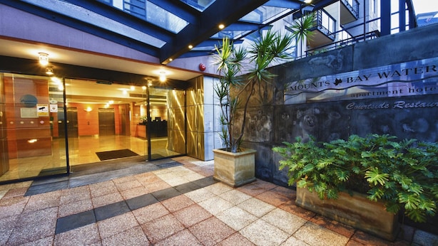 A hotel entrance with a glass door, a sign for 'Mounts Bay Water Apartments Hotel', and a courtyard with potted plants. - Nesuto Mounts Bay (Perth)