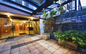 A hotel entrance with a glass door, a sign for 'Mounts Bay Water Apartments Hotel', and a courtyard with potted plants. - Nesuto Mounts Bay (Perth)