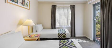A hotel room with two beds, a window with curtains, a lamp, and a framed picture on the wall.