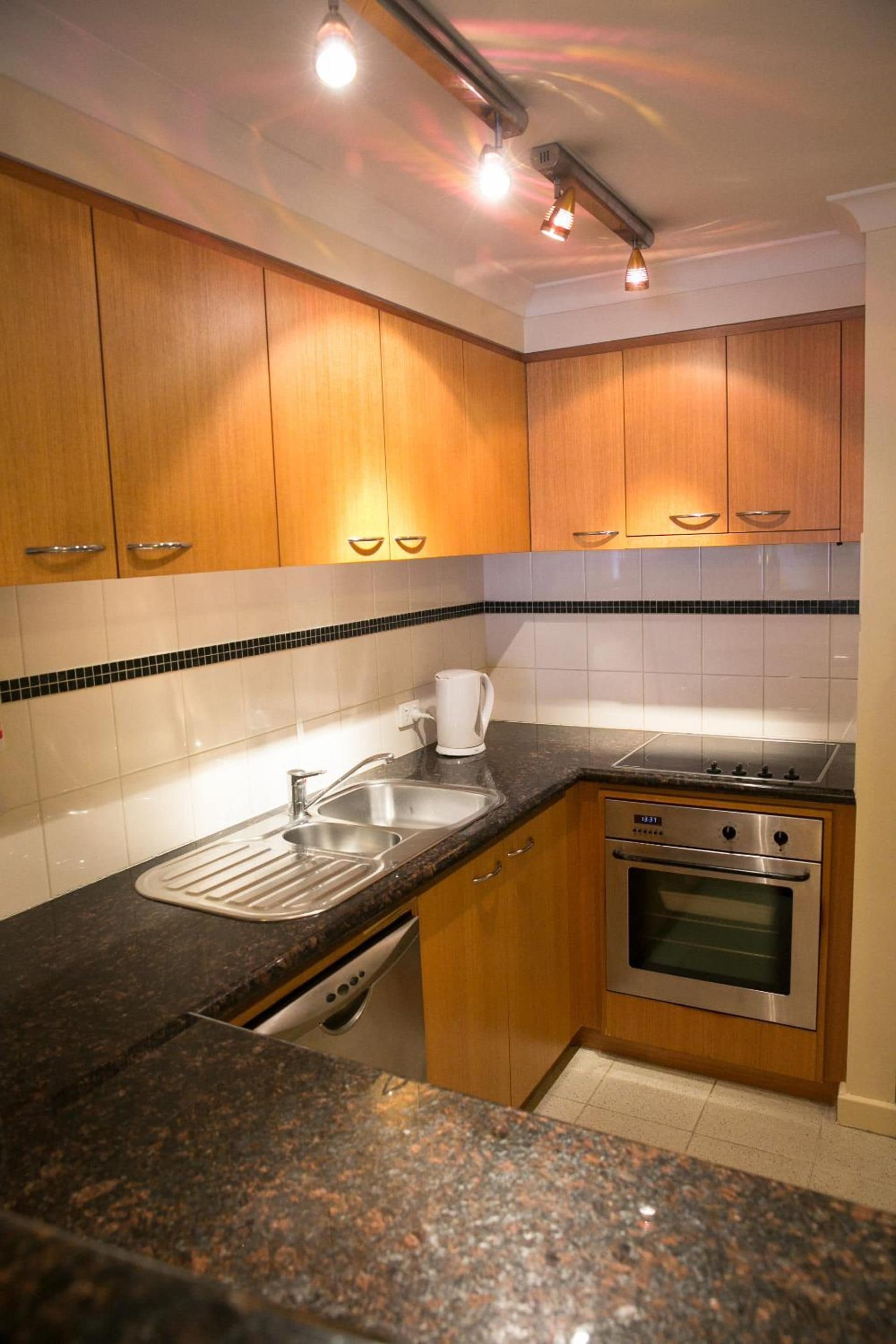 A kitchen with wooden cabinets, a granite countertop, a stainless steel sink, a coffee maker, and a built-in oven.