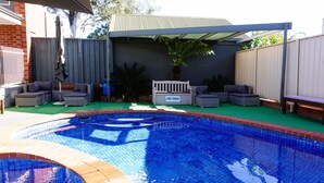 A backyard with a swimming pool, outdoor furniture, and a covered seating area. - Golden Reef Motor Inn (Strathdale)