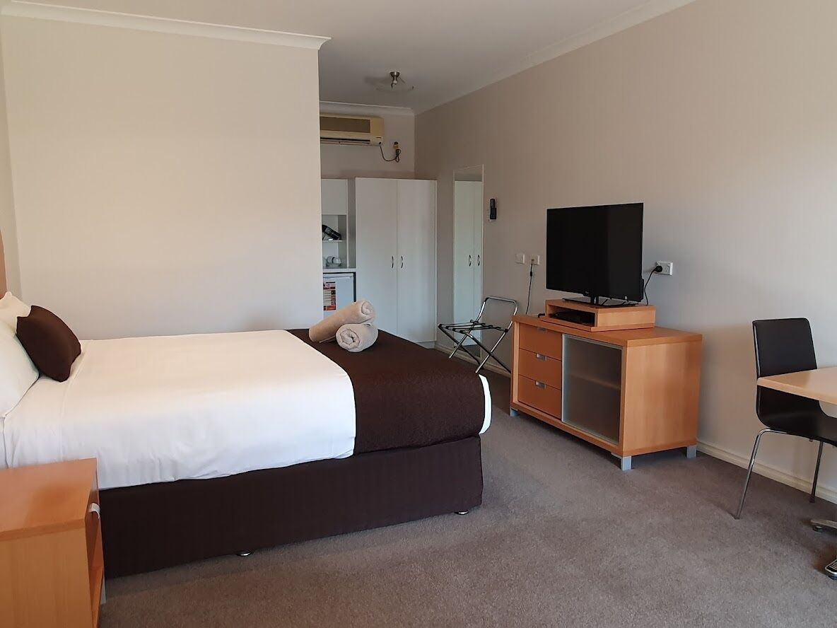 Une chambre d’hôtel avec un lit, un téléviseur posé sur un meuble en bois, un bureau et une armoire.