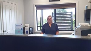 A reception desk with a framed picture above it, a window with blinds, and a door to the left. - Golden Reef Motor Inn (Strathdale)