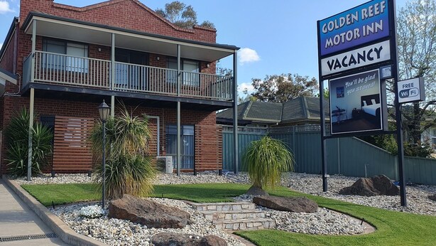 A two-story motel with a balcony, a sign indicating a vacancy, and a small garden area with rocks and plants. - Golden Reef Motor Inn (Strathdale)