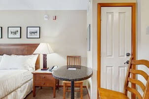 Habitación de hotel con cama, escritorio con lámpara, silla, mesa redonda y una puerta.