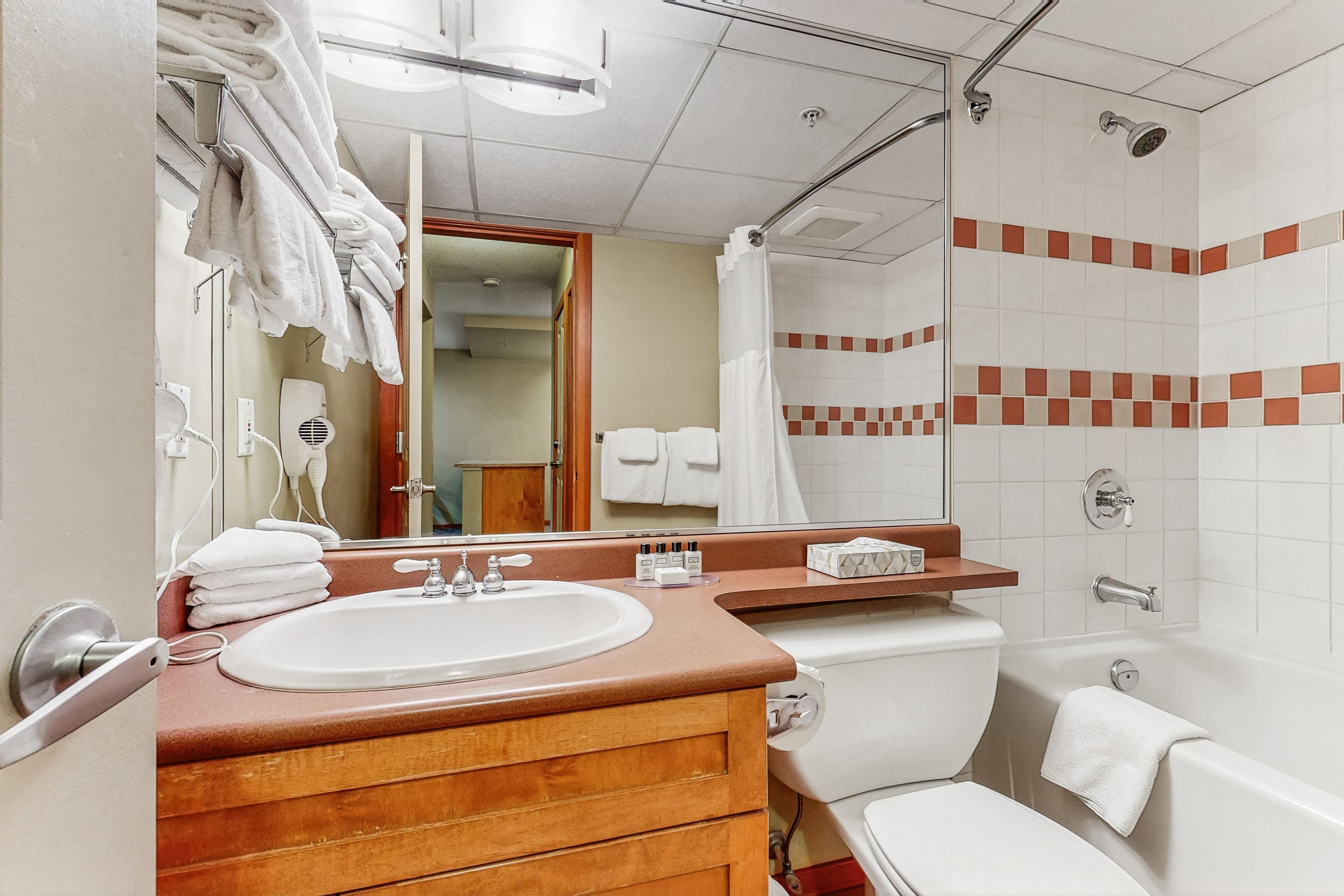 Une salle de bain avec un meuble-lavabo en bois, un lavabo blanc, un miroir, une douche avec une porte en verre et des toilettes.