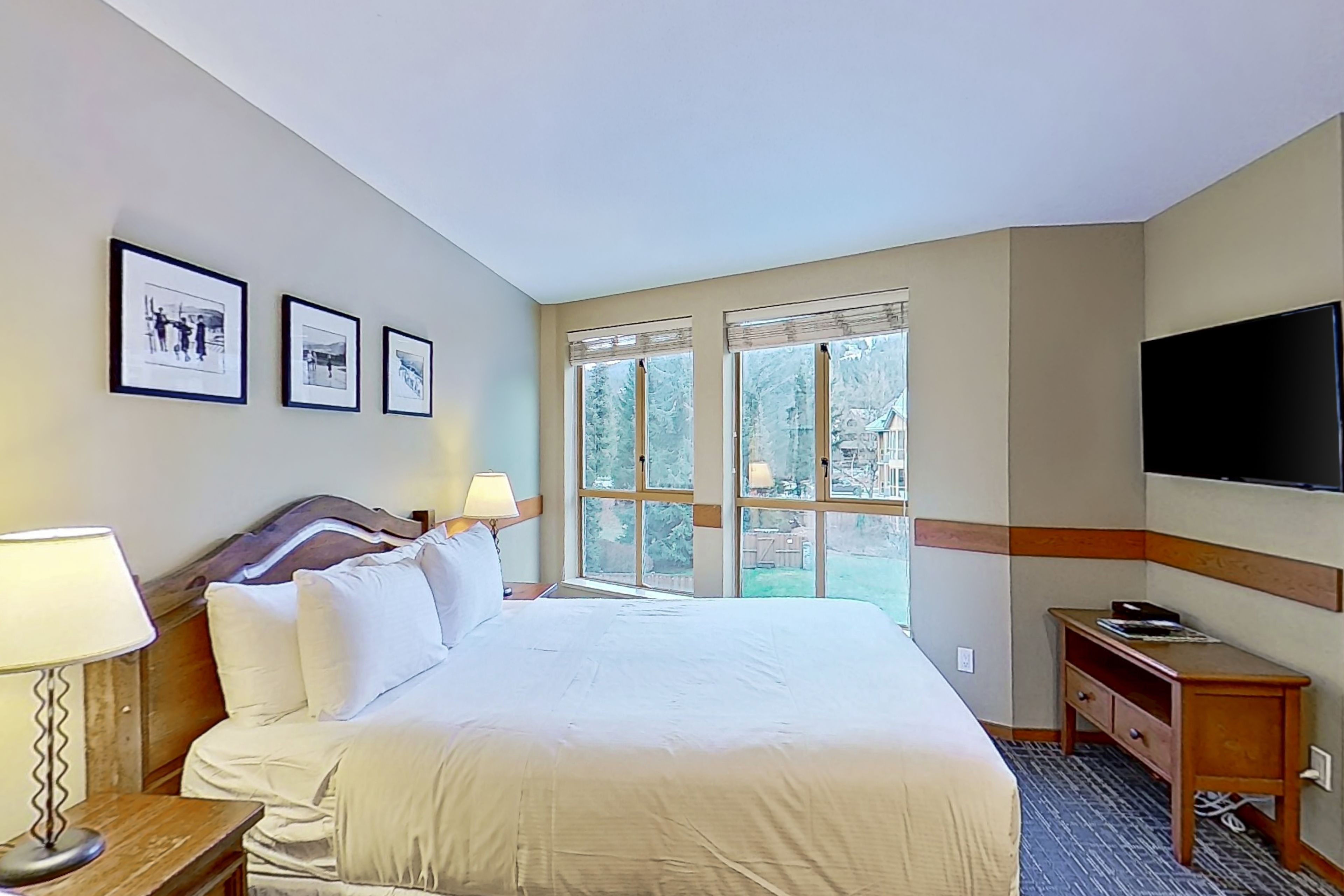A hotel room with a large bed, two bedside lamps, a flat-screen TV, and framed pictures on the wall.