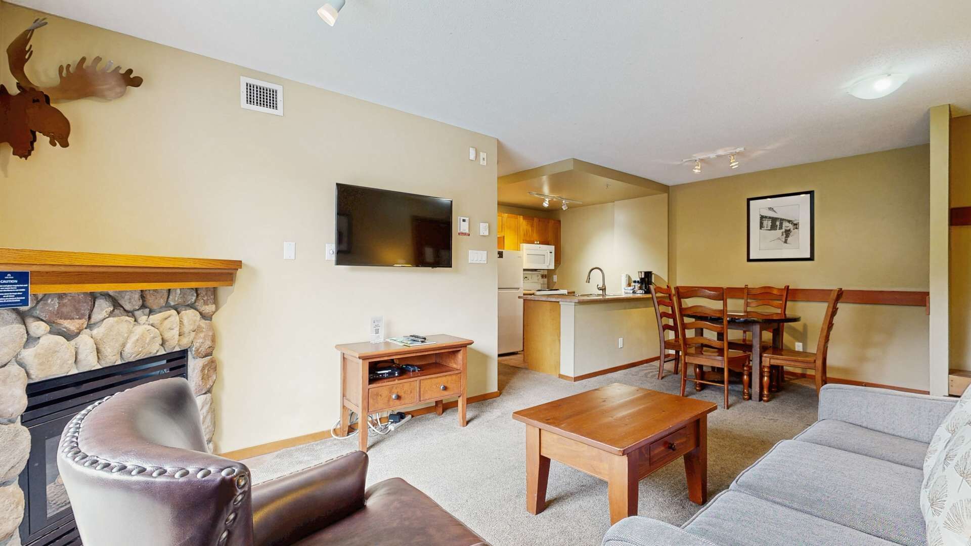 A living room with a fireplace, a television, a dining area with a table and chairs, and a kitchen in the background.