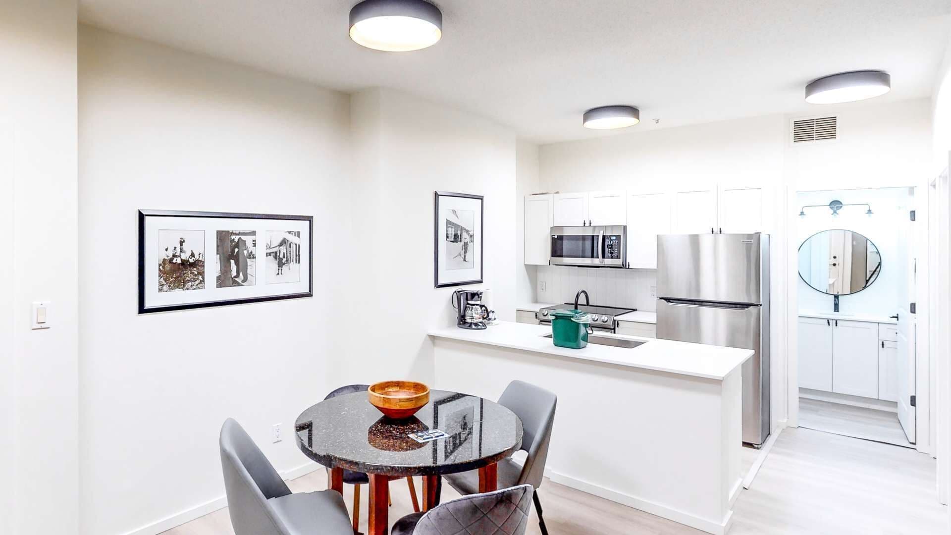 A modern kitchen with white cabinets, stainless steel appliances, and a dining area with a round table and chairs.