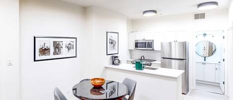 A modern kitchen with white cabinets, stainless steel appliances, and a dining area with a round table and chairs.