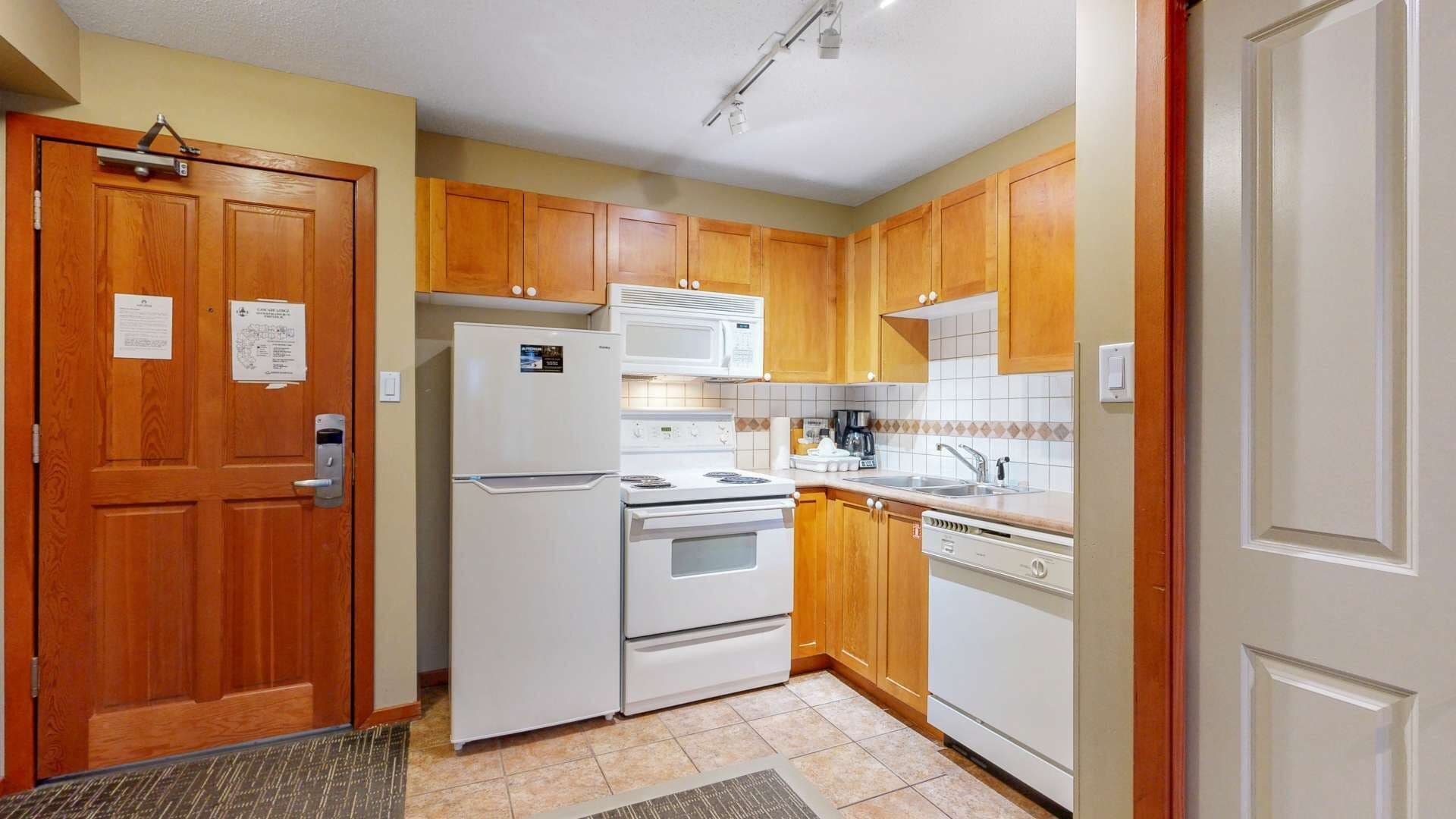 A compact kitchen with wooden cabinets, a refrigerator, stove, microwave, and dishwasher.