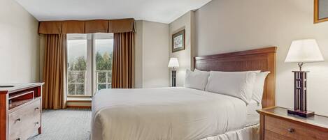 Una habitación de hotel con una cama grande, dos mesitas de noche con lámparas, un aparador de madera y una ventana con cortinas.