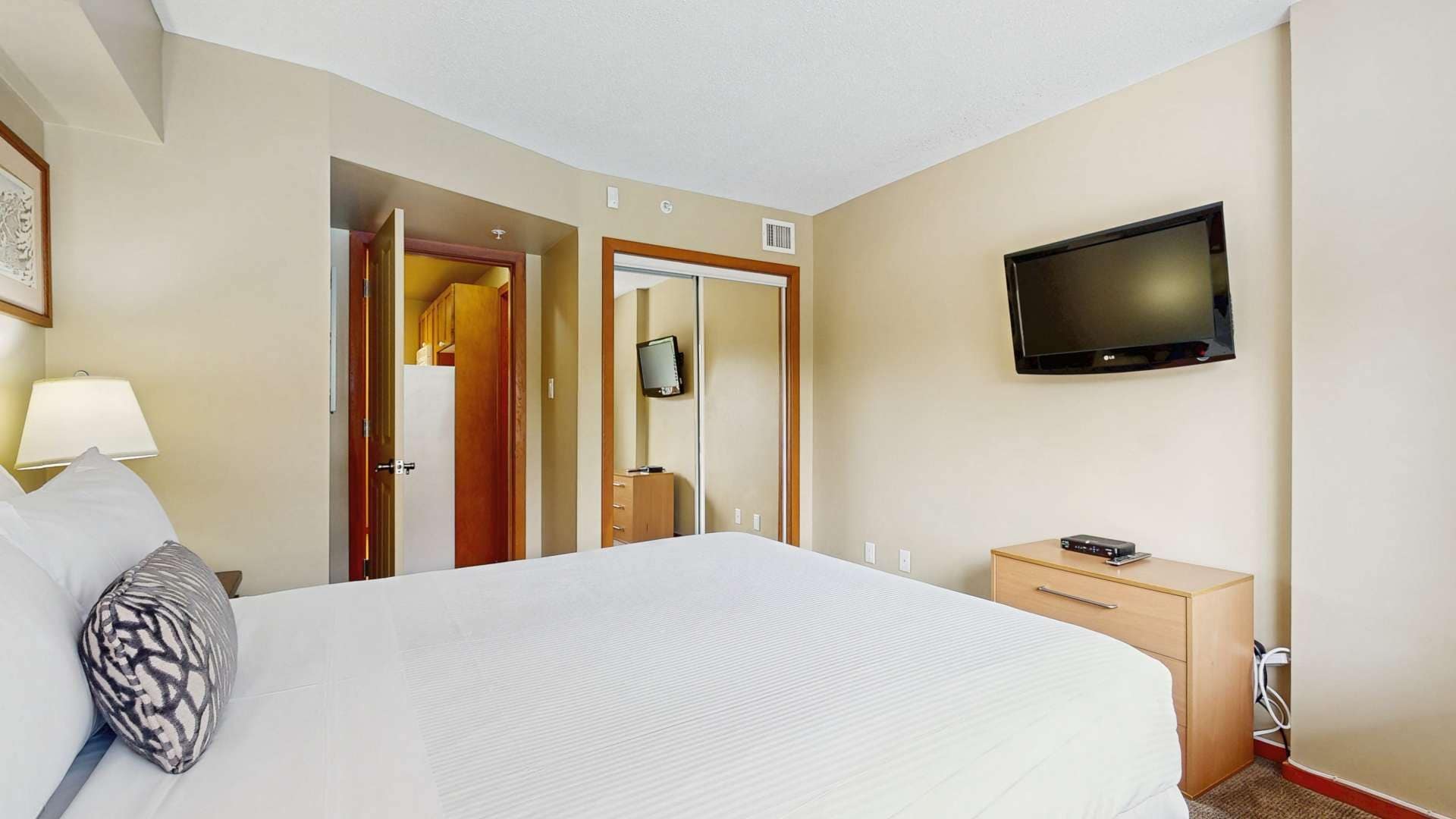 Une chambre d’hôtel comprenant un lit, un téléviseur fixé au mur, un bureau avec une lampe et une armoire.