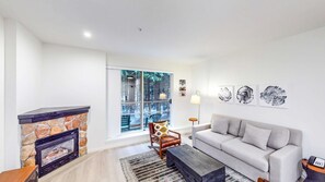 A living room with a stone fireplace, a sofa, a coffee table, and a large window with a view of trees.