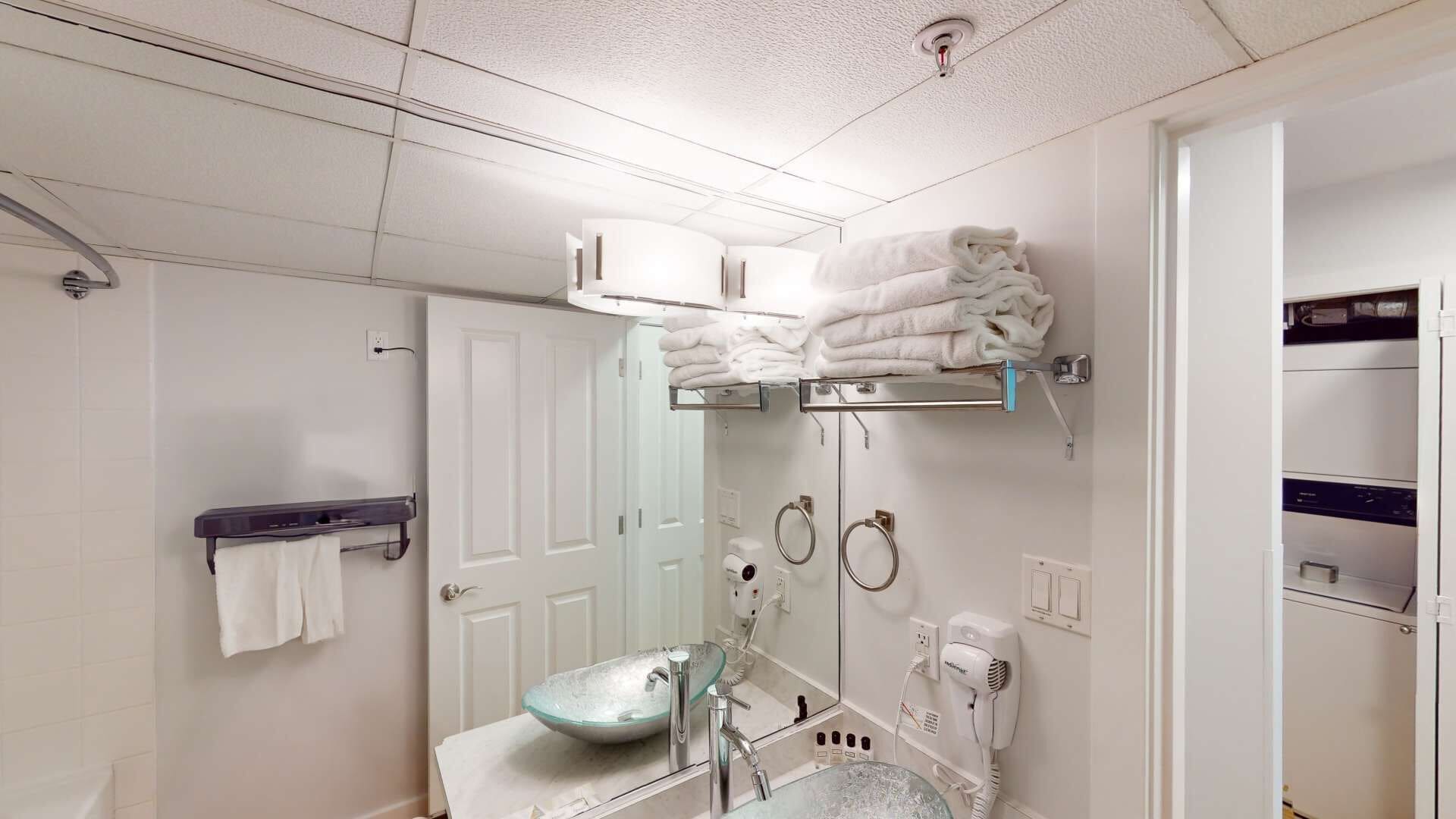 A modern bathroom with a glass sink, towel rack, and a hairdryer.