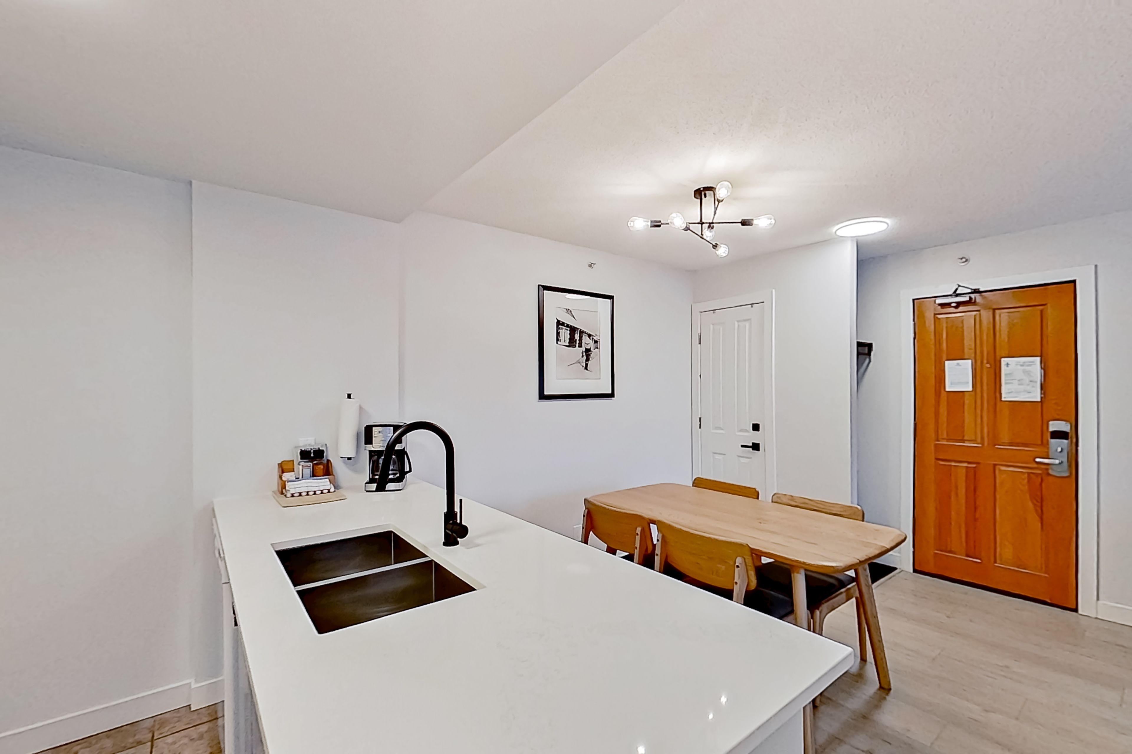 A compact kitchen with a sink, a coffee machine, and a dining area with a wooden table and chairs.