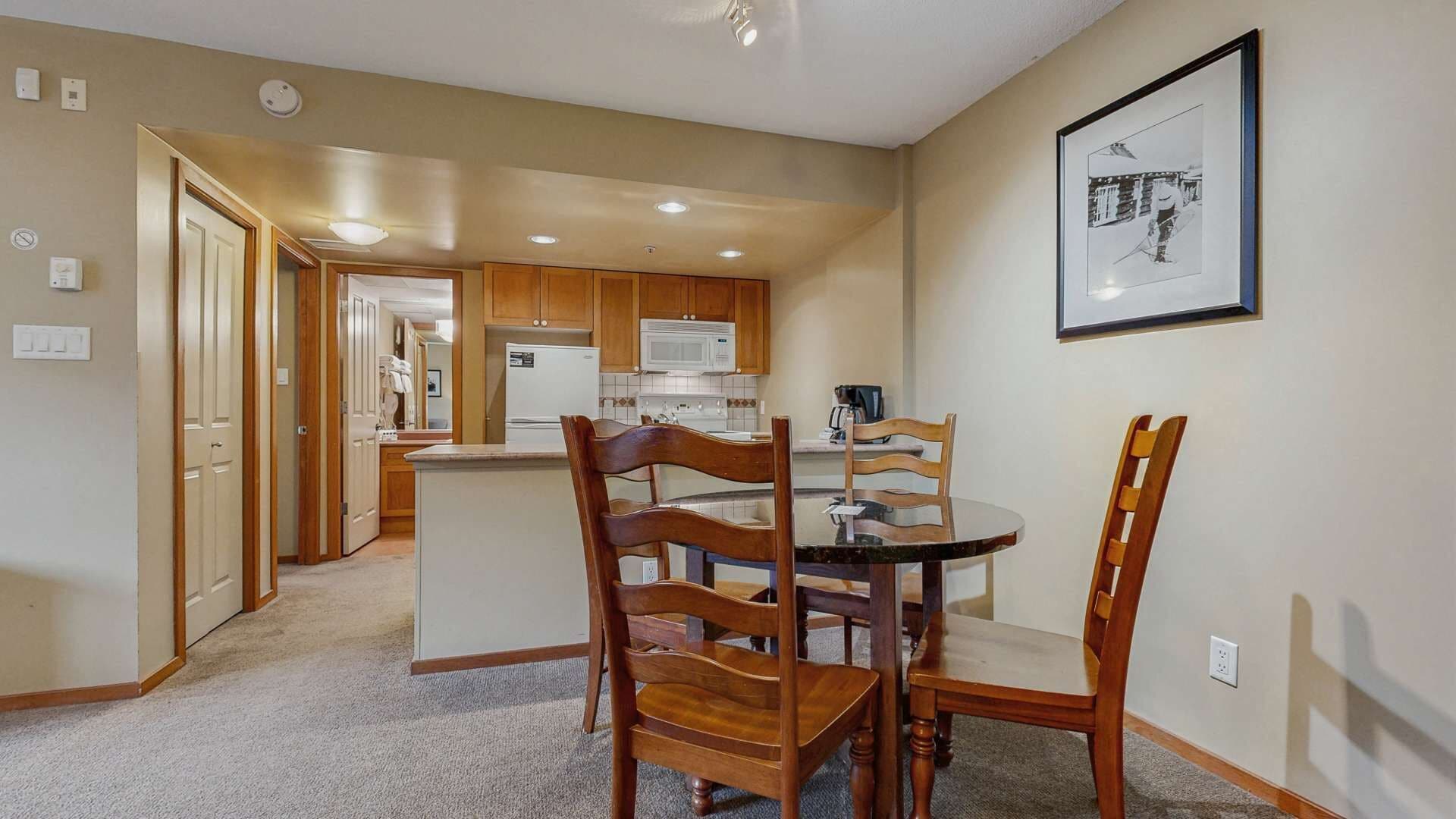 A compact kitchen with wooden cabinets, a microwave, and a dining area with a round table and wooden chairs.