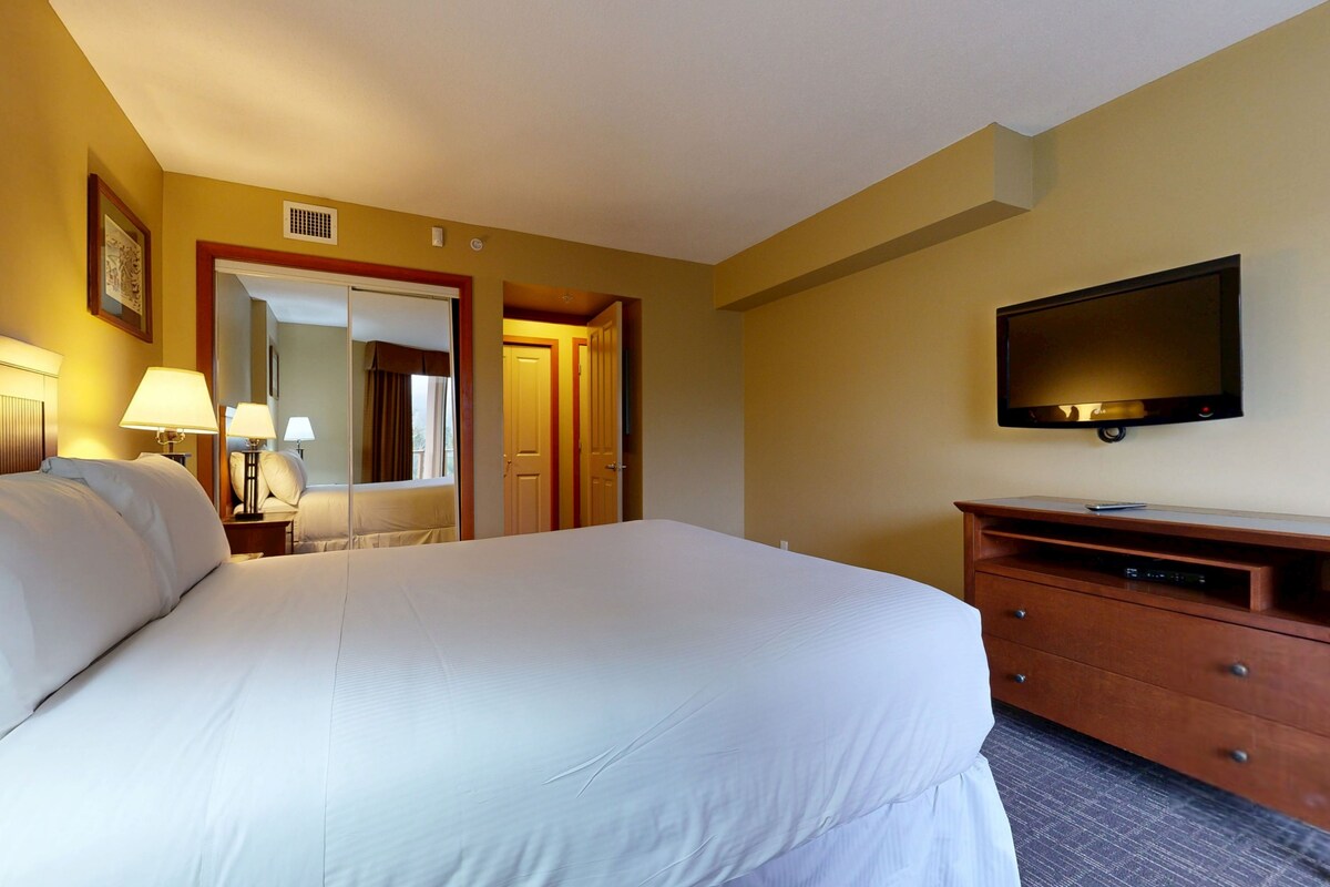 A hotel room with a large bed, a TV on a wooden dresser, and a mirror on the wall.
