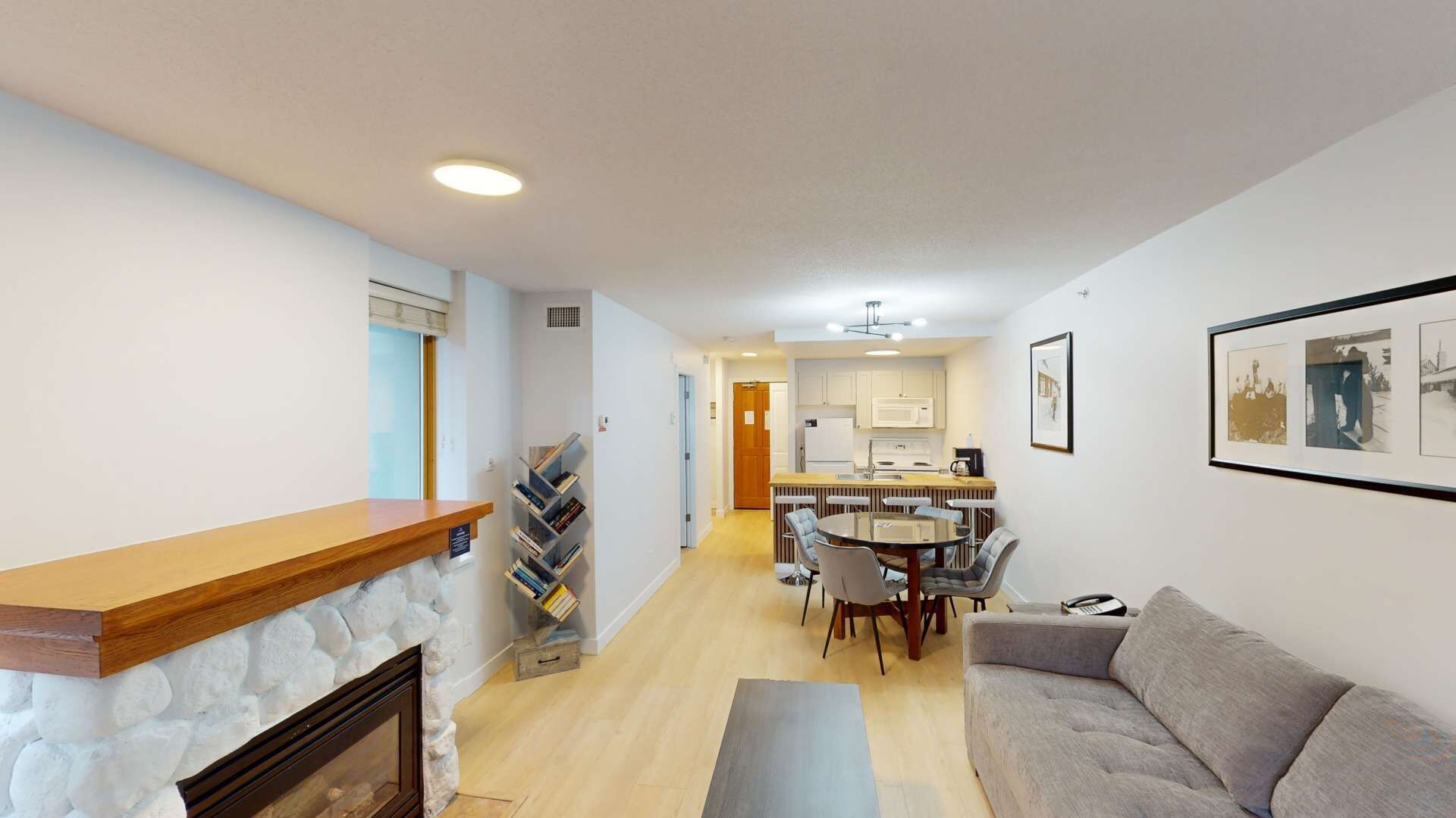 A modern living room with a fireplace, a dining area with a table and chairs, and a kitchen in the background.