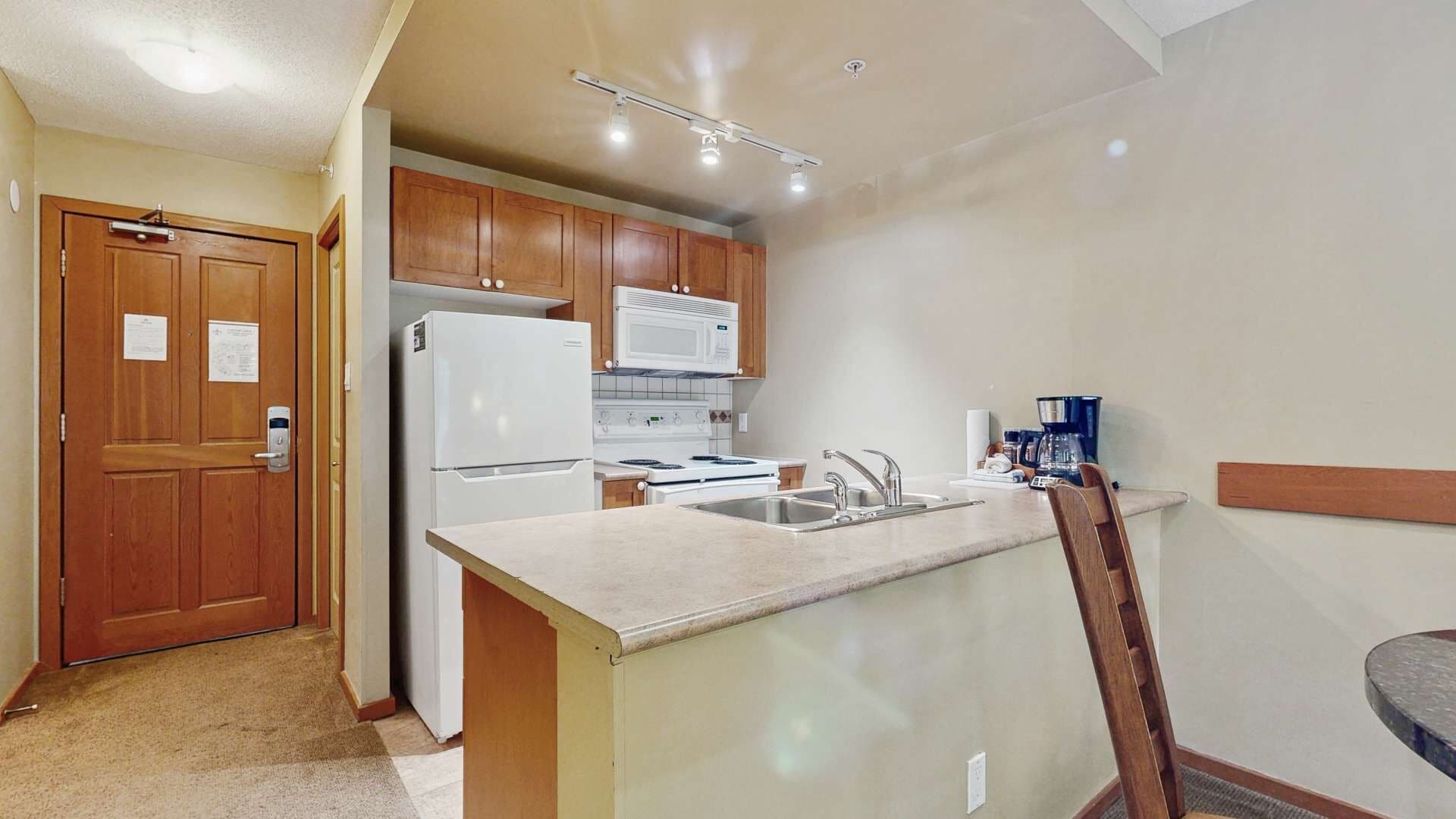 A compact kitchen with wooden cabinets, a white refrigerator, a microwave, and a stove.