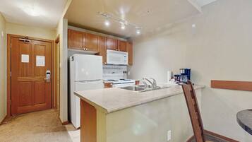 A compact kitchen with wooden cabinets, a white refrigerator, a microwave, and a stove.