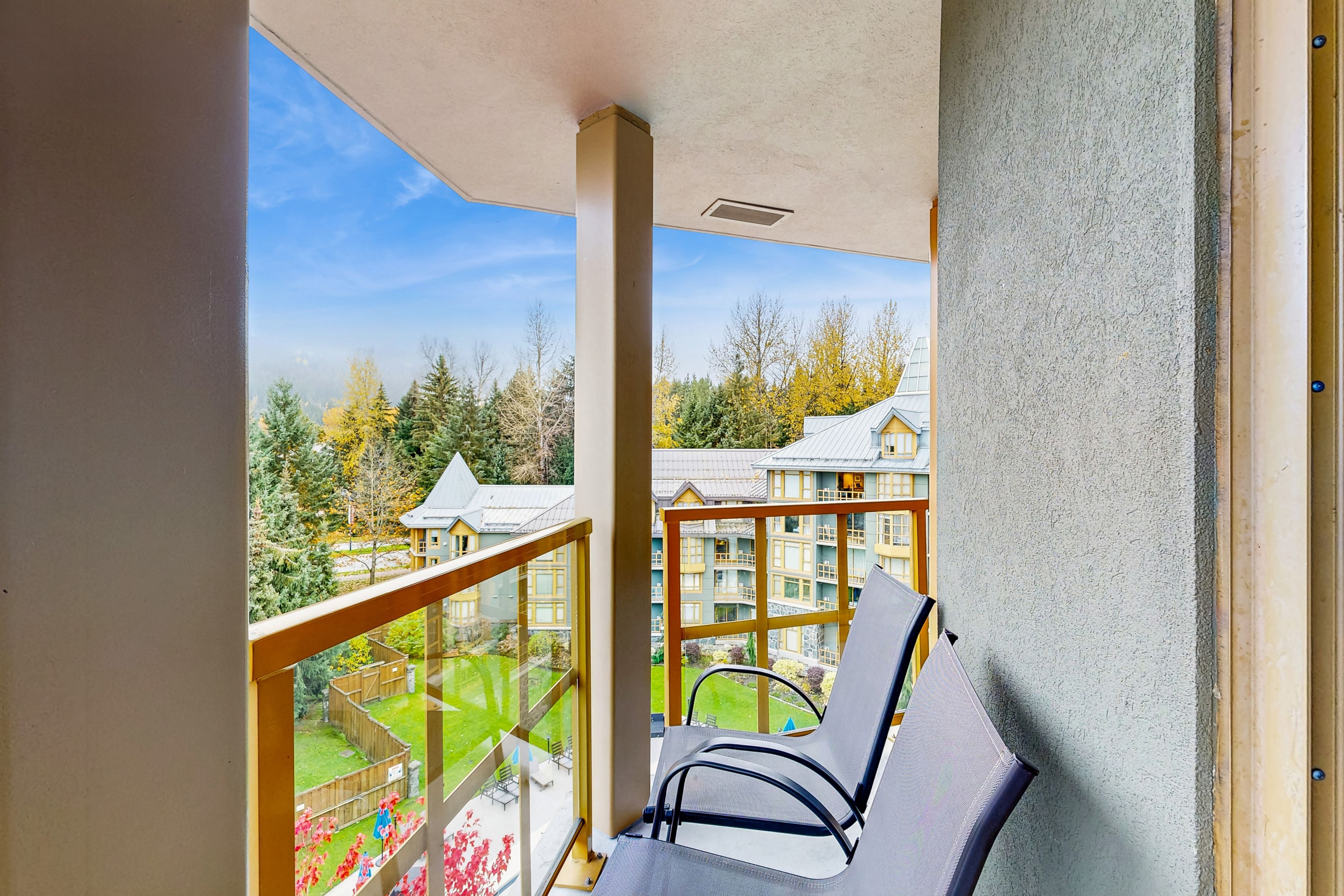 A balcony with two chairs, a wooden railing, and a view of a building complex with multiple balconies.