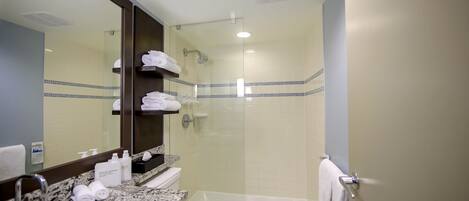 Un baño con lavamanos, espejo, toallero y zona de ducha.